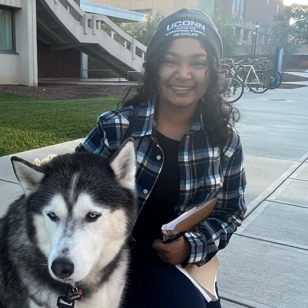 Photo of Sanjana Krishnakumar wearing a UConn Center for International Students and Scholars hat, smiling enthusiastically while standing with Jonathan the Husky.