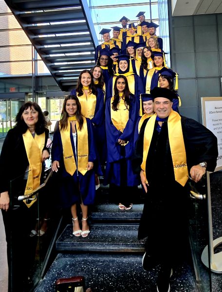 Doctors Radmila Filipovic and Payam Andalib standing proudly with the IONM class of 2025 in UConn graduation attire, standing on the staircase in the Pharmacy building.