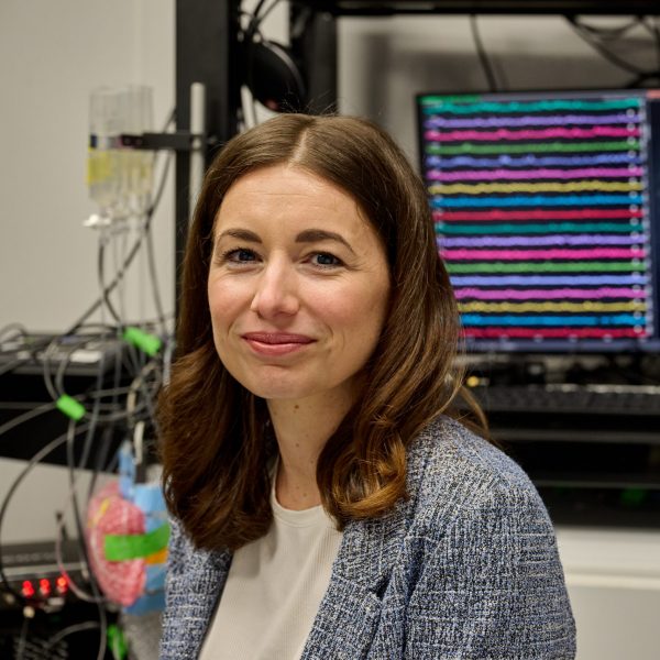 Dr. Natale Sciolino standing in front of wires and a computer screen displaying many lines of colorful recordings.