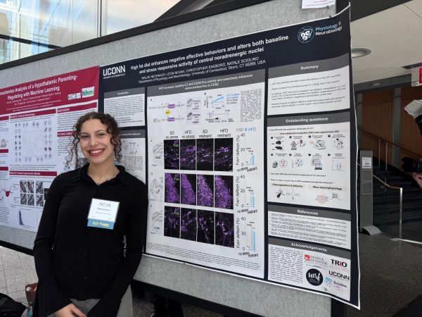 Photo of Malak Nechnach wearing a black long sleeve blouse, standing proudly in front of a scientific research poster.